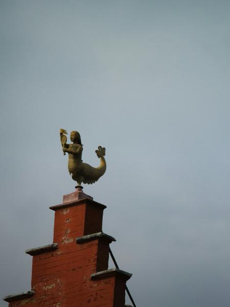 Golden mermaid weather vane atop a brick building